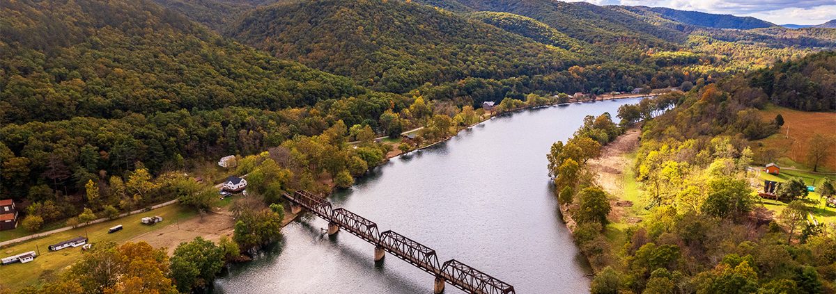 This is an image of a river with a trail bridge surrounded by mountains with fall foliage.