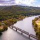 This is an image of a river with a trail bridge surrounded by mountains with fall foliage.