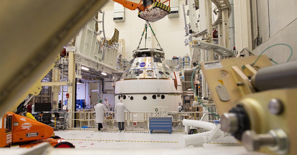 A crane returns NASA’s Artemis II Orion spacecraft to the Final Assembly and System Testing (FAST) cell inside the Neil A. Armstrong Operations and Checkout Building at NASA’s Kennedy Space Center in Florida on Friday, March 21, 2025, following installation of four solar array winds and adapter jettison fairings. Once complete, the Orion spacecraft will be transported to other facilities for fueling and integration with its launch abort system before arriving at the Vehicle Assembly Building where it will be stacked atop the SLS (Space Launch System) by NASA’s Exploration Ground System team at the Vehicle Assembly Building in preparations for Artemis II launch operations.
