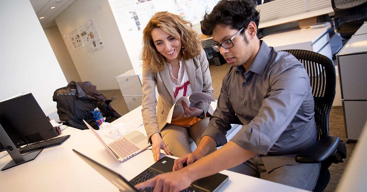 A professor and a student work together on a laptop in a classroom